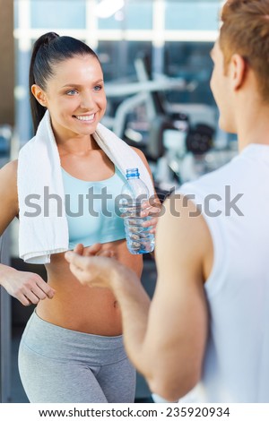 Sporty couple in gym. Beautiful young sporty couple talking and smiling while standing in gym