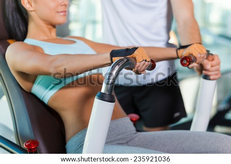 Training with instructor. Close-up of beautiful young woman working out in gym while instructor supporting her