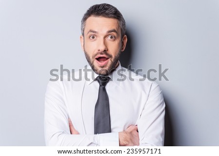Unbelievable news! Portrait of surprised mature man in shirt and tie keeping mouth open and looking at camera while standing against grey background