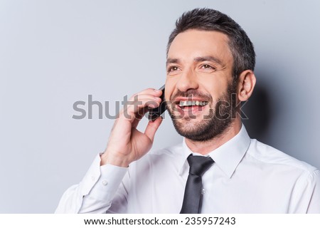 Great news! Happy mature man in shirt and tie talking on the mobile phone and smiling while standing against grey background