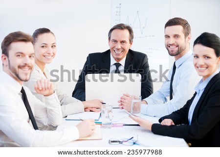 Confident business team. Group of confident business people in formalwear sitting at the table together and smiling