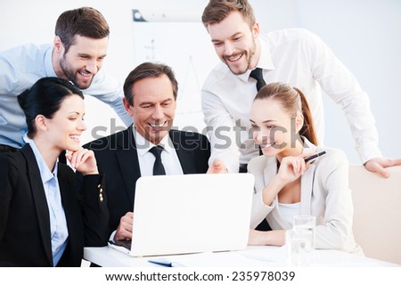 Business discussion. Group of confident business people in formalwear sitting at the table together and discussing something while looking at the laptop