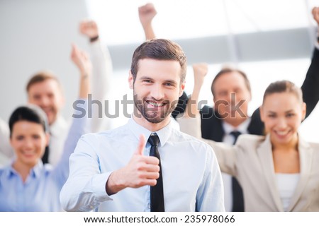 Feeling confident in his team. Happy businessman showing his thumb up and smiling while his colleagues standing in the background