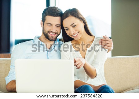 Surfing the net together. Beautiful young loving couple sitting together on the couch and looking at laptop