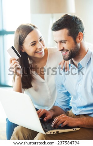 Shopping online together. Beautiful young loving couple shopping online together while woman holding credit card and smiling