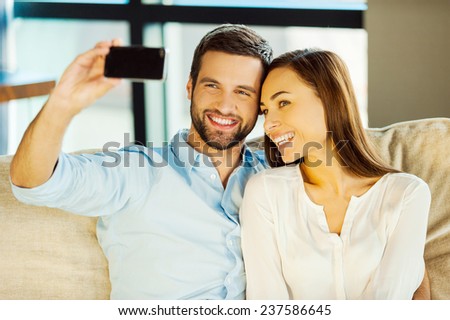 Capturing love. Beautiful young loving couple bonding to each other and making selfie while sitting on the couch together