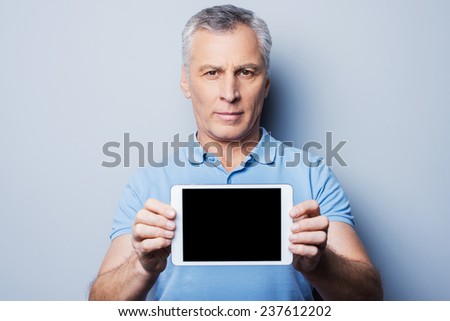 Copy space on his tablet. Confident senior man showing his digital tablet and smiling while standing against grey background