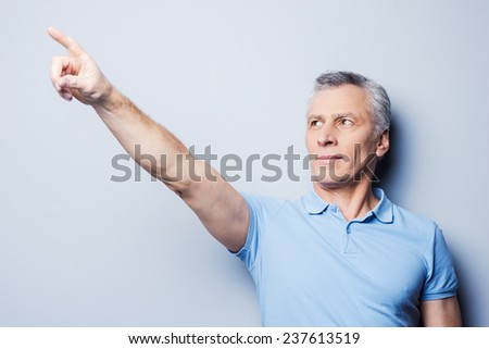 Look over there! Handsome senior man pointing away while standing against grey background