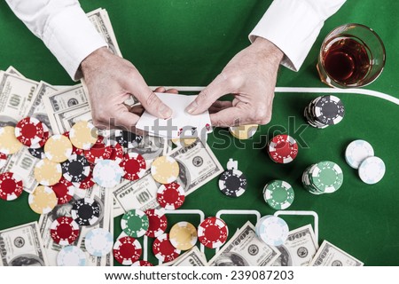 Good luck. Top view of man holding cards while sitting at the poker table with lots of chips and money laying on it