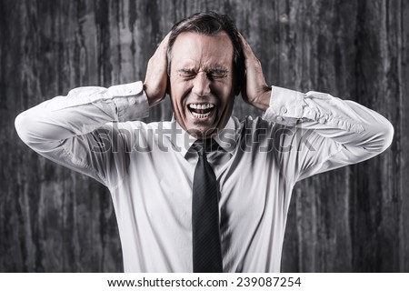 Emotional stress. Stressed mature man in shirt and tie holding head in hands and shouting while standing in front of dirty wall
