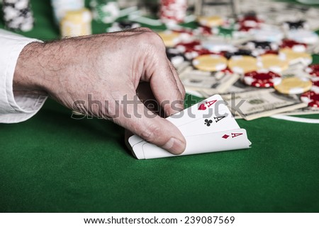 Nice combination. Close-up of male hand showing his cards on the poker table with chips and money laying in the background