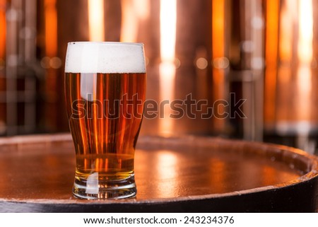 Fresh beer. Close-up of glass with beer standing on the wooden barrel with metal containers in the background