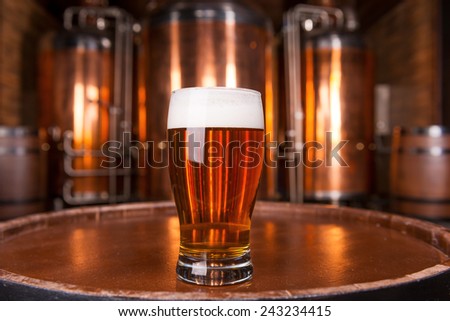 The best beer in town. Close-up of glass with fresh beer standing on the wooden barrel with metal container in the background