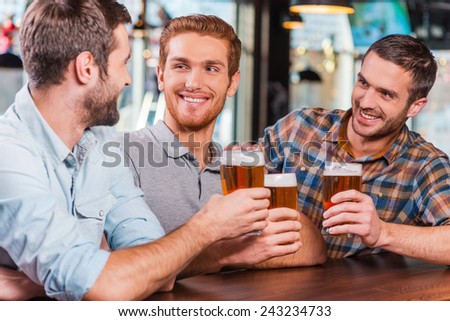 Relaxing after work. Three happy young men in casual wear talking and drinking beer while sitting at the bar counter together