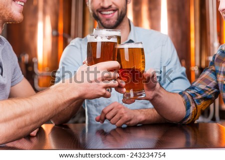 Old friends meeting. Close-up of three happy young men in casual wear toasting with beer while sitting in beer pub together
