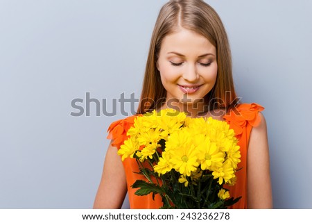 Beautiful tenderness. Beautiful young woman in pretty dress holding bouquet of flowers while standing against grey background