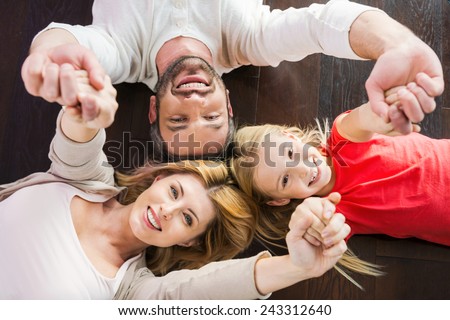 Happy family together. Top view of happy family of three bonding to each other and smiling while lying on the hardwood floor