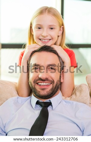 Me and my father. Cute little girl bonding to her cheerful father sitting on the couch at home