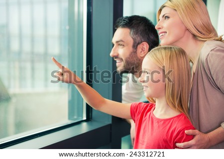Is it a plane? Happy family of three bonding to each other and smiling while looking through a window together