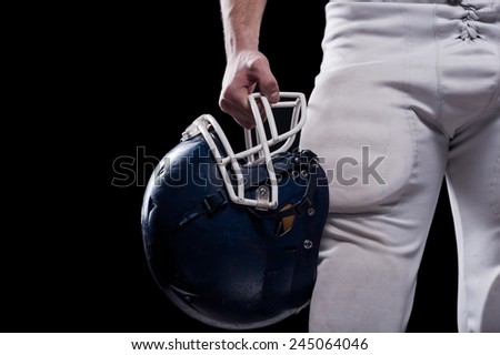 Crash helmet.  Cropped image of American football player holding football helmet while standing against black background