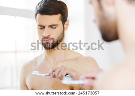 Feeling displeased with his new toothbrush. Rear view of frustrated young beard man looking at his toothbrush and expressing negativity while standing against a mirror