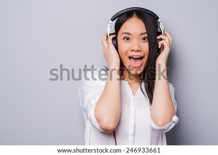 Love this song. Beautiful young Asian holding hands on headphones and looking at camera while standing against grey background