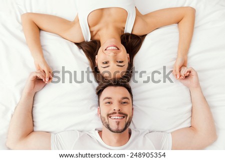 Relaxing in bed together. Top view of beautiful young loving couple lying in bed together and holding hands