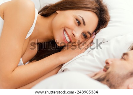 Good morning! Top view of beautiful young loving couple lying in bed and looking at each other with smile