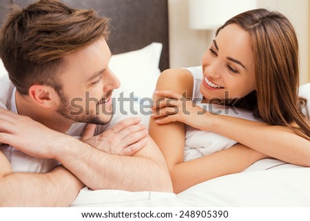 Enjoying time together. Beautiful young loving couple lying in bed together and looking at each other with smile