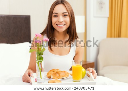 Good morning starts from breakfast in bed. Beautiful young woman having breakfast in bed and smiling