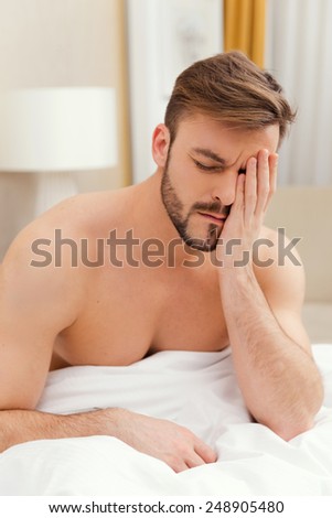 Early wake up. Depressed young man sitting in bed and touching face with hand