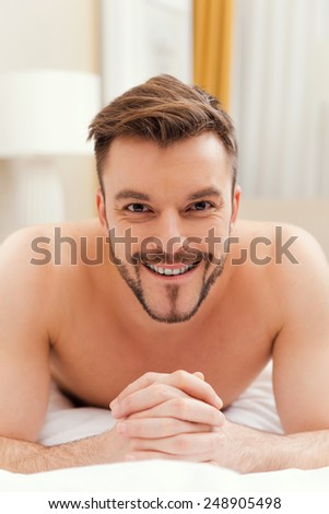 Handsome in bed. Handsome young shirtless man lying in bed and smiling