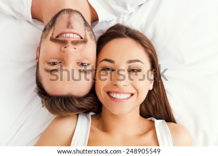 Happy loving couple. Top view of beautiful young loving couple lying in bed together and smiling