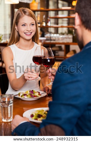 Celebrating their anniversary. Beautiful young loving couple toasting with red wine and smiling while sitting at the restaurant together