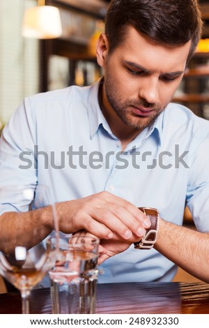 She is late again. Frustrated young man checking the time while sitting at the restaurant