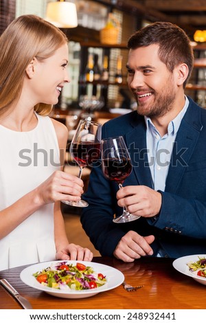 Cheers to us! Beautiful young loving couple toasting with red wine and smiling while sitting at the restaurant together