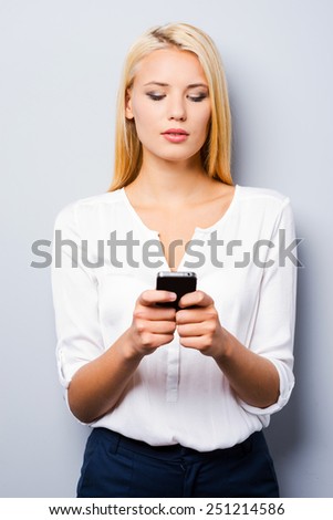 Typing a message for you. Beautiful young blond hair women holding mobile phone and looking at it while standing against grey background