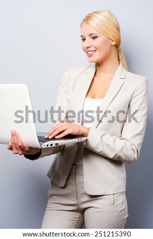 In love with her work. Confident young businesswoman holding laptop while standing against grey background