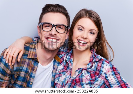 Bright smile for whole life! Beautiful young loving couple smiling at camera while standing against grey background