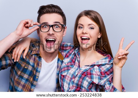 Hey, enough of sad! Beautiful young loving couple gesturing and smiling at camera while standing against grey background