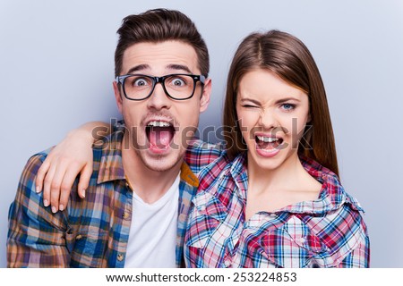 Playful couple. Beautiful young loving couple making faces at camera while standing against grey background