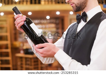 Choosing the best wine. Close-up of confident young man in waistcoat and bow tie examining wine bottle