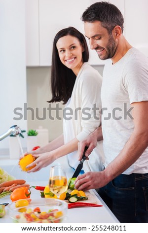 Cooking together is fun. Beautiful young loving couple cooking together while standing in the kitchen
