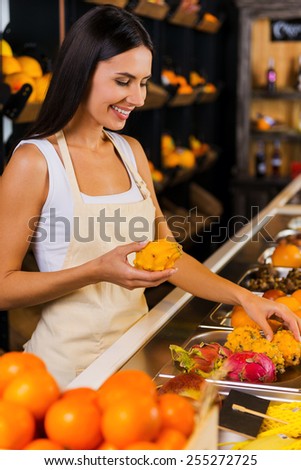 Working in fruit paradise. Beautiful young woman in apron working in grocery store with variety of fruits in the background
