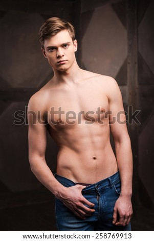 Confident in his perfect body. Handsome young muscular man posing while standing against metal background