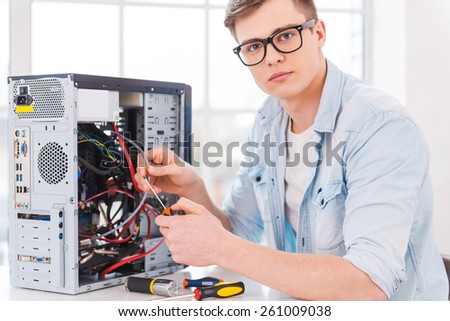 Smart professional. Portrait of handsome young man repairing computer while sitting at his working place