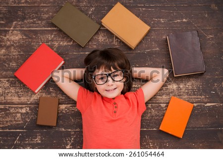 I love studying! Top view of a little boy lying on the floor and smiling while books laying all around him