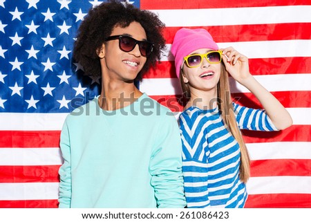 American dreams. Funky young couple wearing sunglasses and smiling while standing against American flag