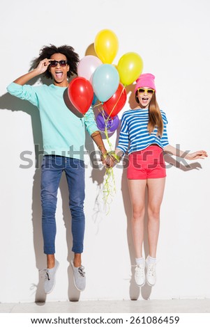 Love in all the colors of rainbows. Funky young couple holding balloons while jumping against white background