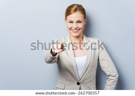 I choose you! Beautiful young businesswoman pointing you while standing against grey background